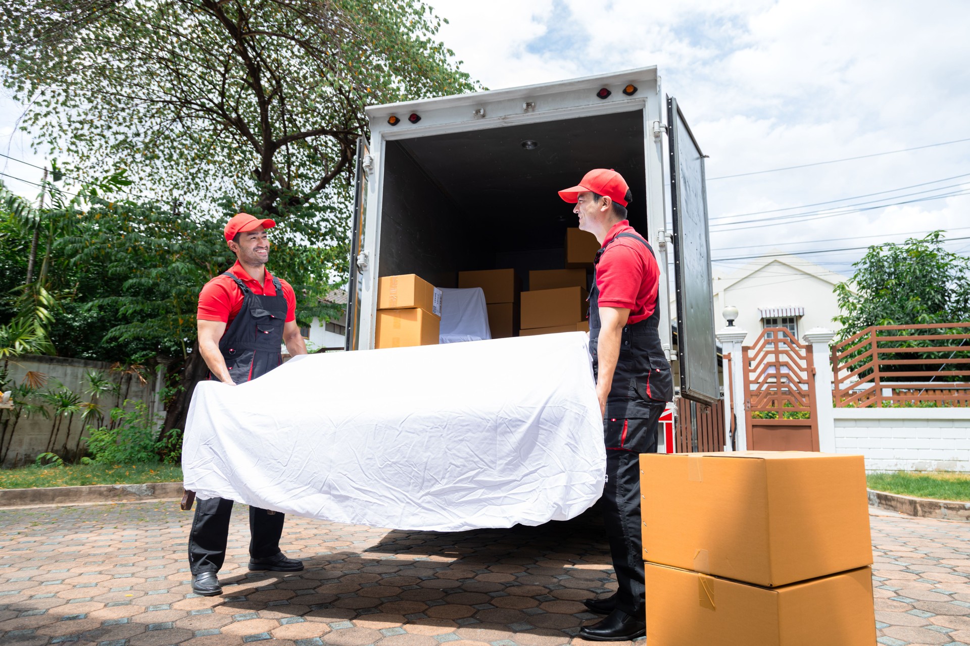 Professional multiethnic house moving employees in uniform working uploading cardboard box and furniture at customer home to new house, teamwork Indian man and Caucasian delivery moving house services